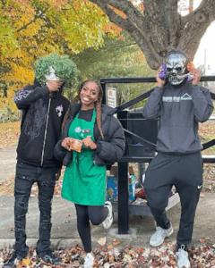 aniyah beck beside two people wearing halloween masks and all black clothes